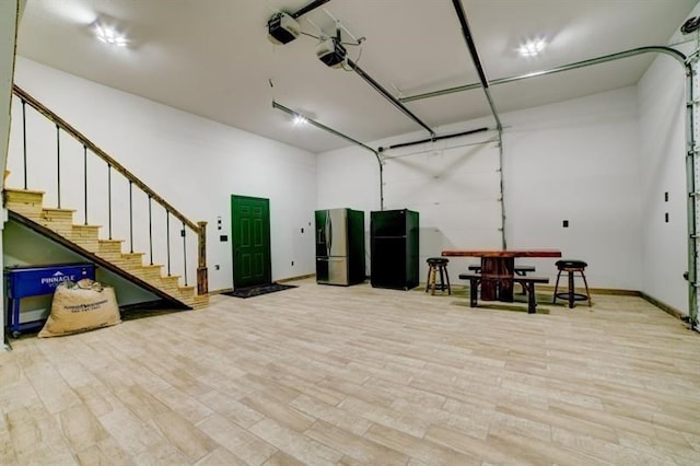 interior space with baseboards, freestanding refrigerator, a garage door opener, and stainless steel fridge with ice dispenser