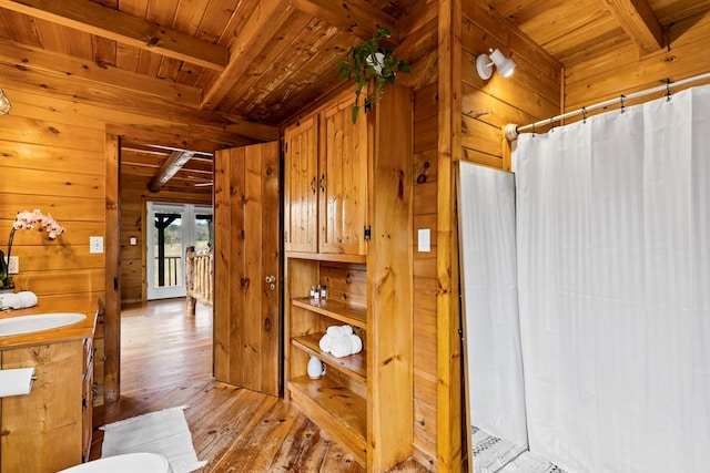 bathroom featuring beam ceiling, hardwood / wood-style floors, wooden walls, wood ceiling, and vanity