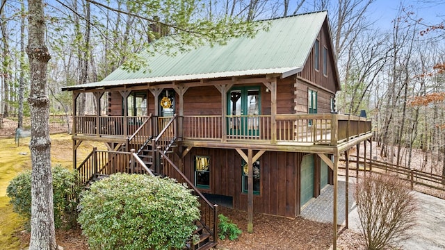 view of front of property featuring driveway, metal roof, an attached garage, log siding, and stairs