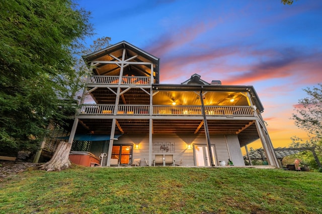 back house at dusk featuring ceiling fan, a patio, a yard, and a hot tub