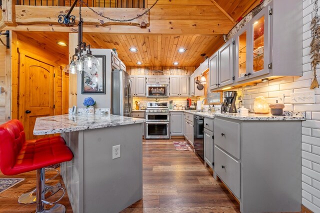 kitchen featuring appliances with stainless steel finishes, a center island, wood ceiling, decorative backsplash, and light stone counters