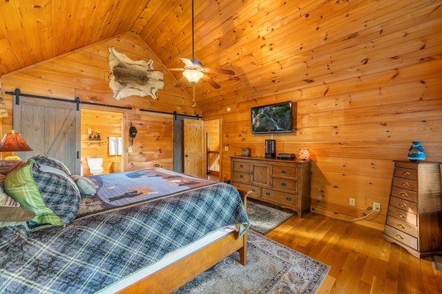 bedroom featuring wood-type flooring, ceiling fan, a barn door, connected bathroom, and lofted ceiling