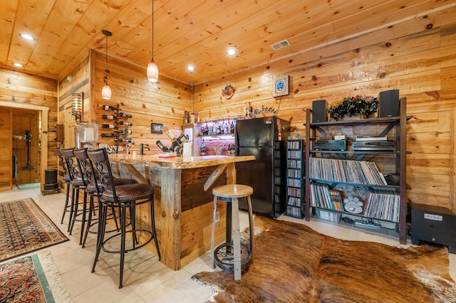 kitchen with wooden ceiling, hanging light fixtures, black fridge, and wooden walls