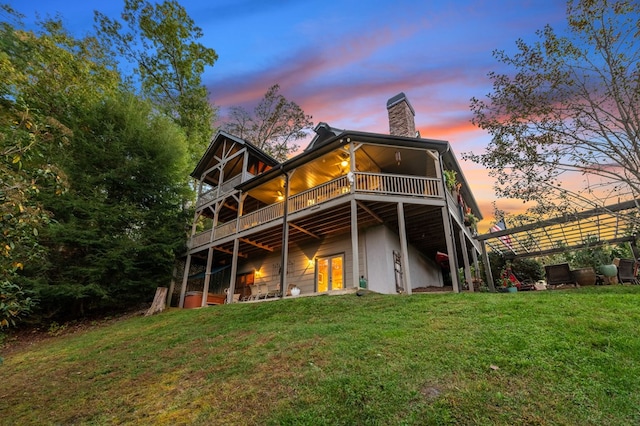 back house at dusk with a lawn and a pergola