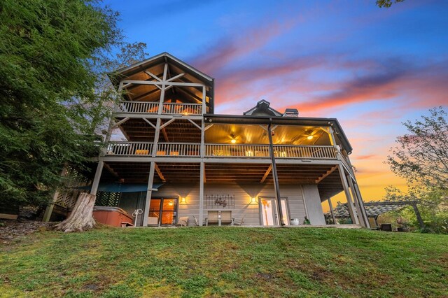 back house at dusk featuring ceiling fan, a wooden deck, a yard, and a hot tub