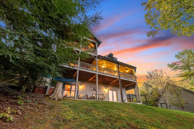 back house at dusk with a patio, a balcony, a lawn, and a hot tub