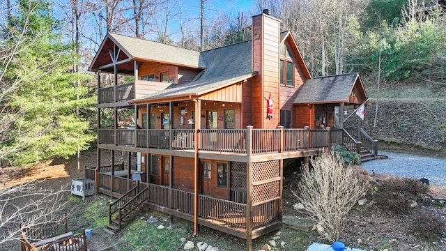 back of house with roof with shingles, a chimney, and a wooden deck