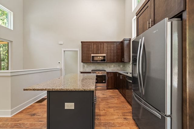 kitchen with light stone countertops, a center island, stainless steel appliances, and dark brown cabinets