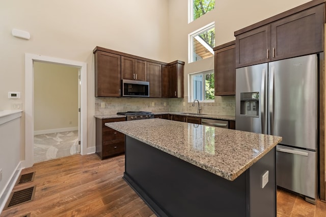 kitchen with appliances with stainless steel finishes, light stone counters, dark brown cabinetry, sink, and a center island