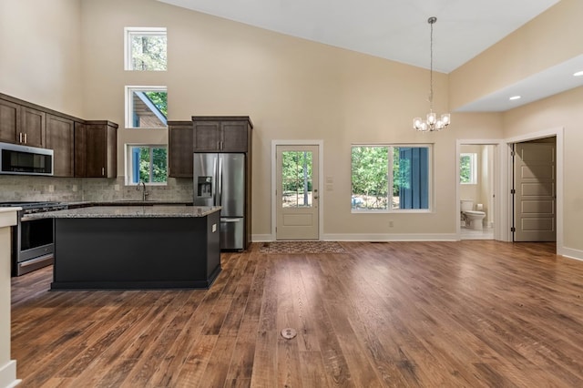 kitchen with a center island, stainless steel appliances, light stone counters, and high vaulted ceiling