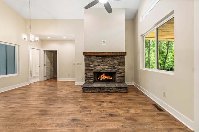 unfurnished living room featuring a fireplace, wood-type flooring, and ceiling fan with notable chandelier