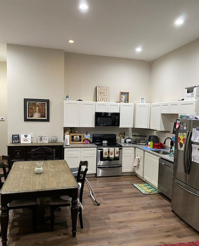 kitchen with sink, dark hardwood / wood-style flooring, light stone counters, white cabinetry, and stainless steel appliances