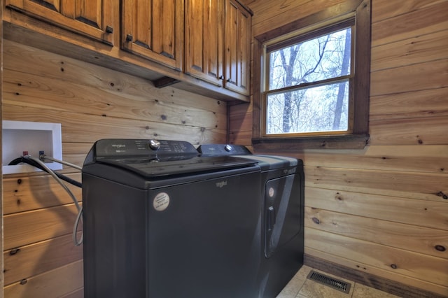 laundry area featuring independent washer and dryer, visible vents, wood walls, and cabinet space