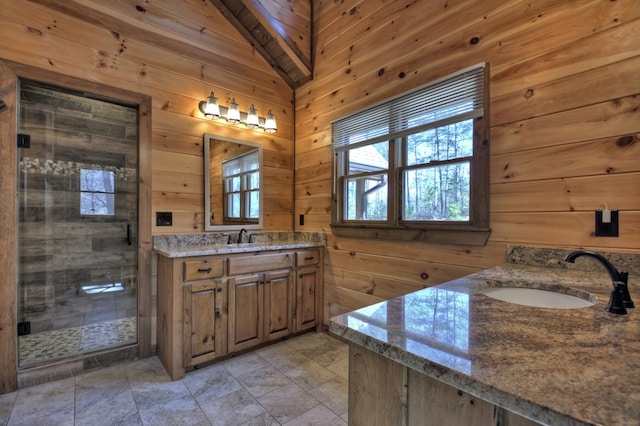 bathroom featuring wood walls, plenty of natural light, a sink, a stall shower, and two vanities