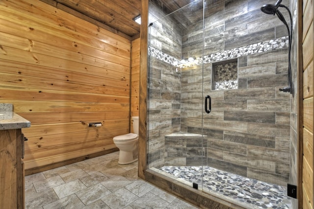 full bath with toilet, vanity, a shower stall, wooden walls, and stone finish floor