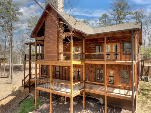 rear view of property with a chimney, a deck, central AC, and roof with shingles