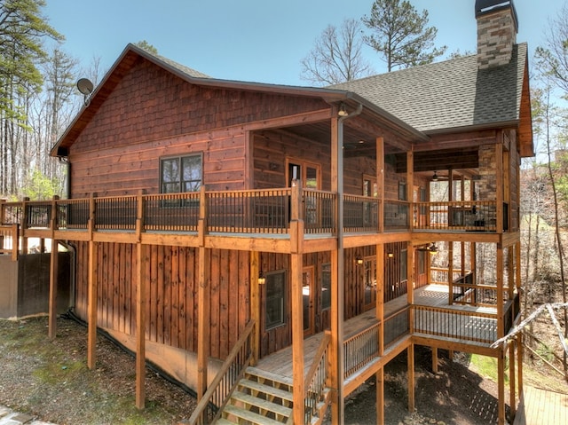 exterior space with a wooden deck, roof with shingles, and a chimney