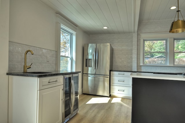 kitchen featuring stainless steel fridge, beverage cooler, sink, pendant lighting, and white cabinetry