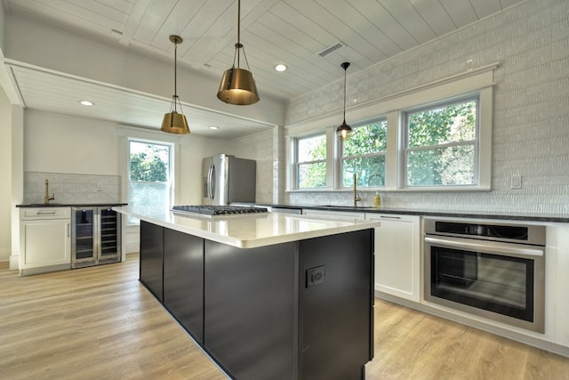 kitchen featuring stainless steel appliances, a kitchen island, white cabinetry, wine cooler, and hanging light fixtures