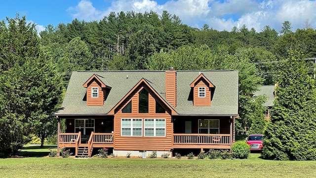 view of front facade featuring faux log siding, covered porch, a chimney, a forest view, and a front lawn