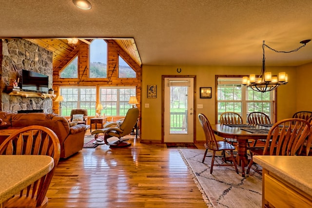 dining room with a notable chandelier, baseboards, vaulted ceiling, light wood-style flooring, and a textured ceiling