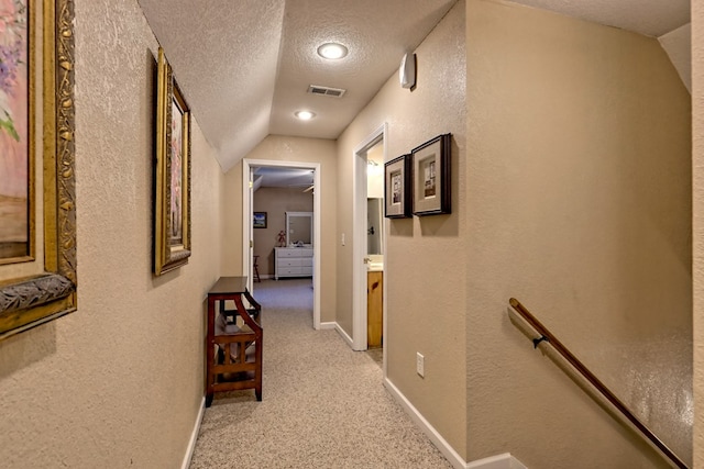 hall featuring a textured ceiling, visible vents, an upstairs landing, lofted ceiling, and a textured wall