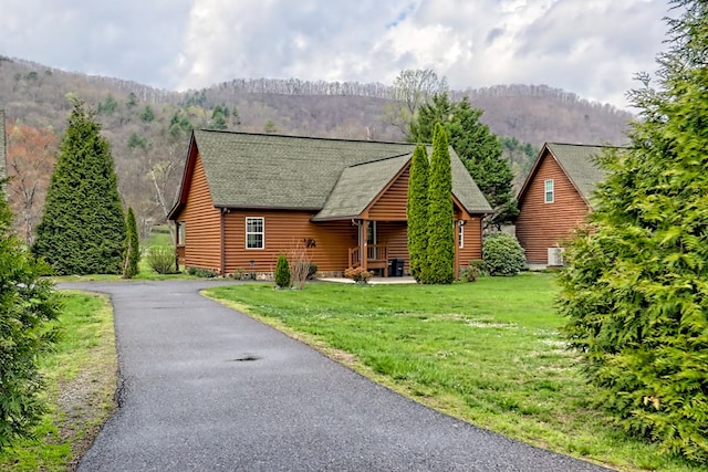 log cabin featuring a mountain view, a front lawn, faux log siding, and roof with shingles