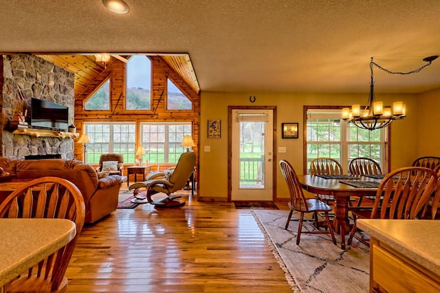 dining room featuring a notable chandelier, light wood-style floors, a fireplace, a textured ceiling, and lofted ceiling