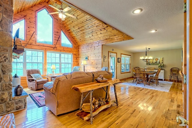 living area with ceiling fan with notable chandelier, high vaulted ceiling, light wood-type flooring, recessed lighting, and wood walls