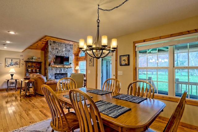 dining space featuring wood-type flooring, a stone fireplace, a notable chandelier, and baseboards