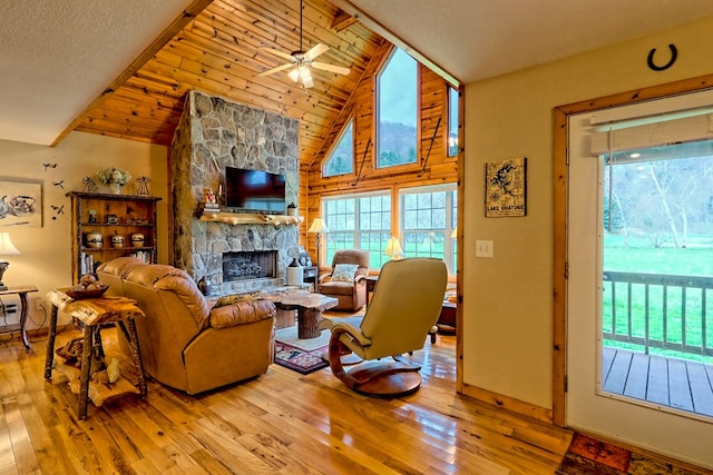 living room featuring hardwood / wood-style floors, high vaulted ceiling, a ceiling fan, and a stone fireplace