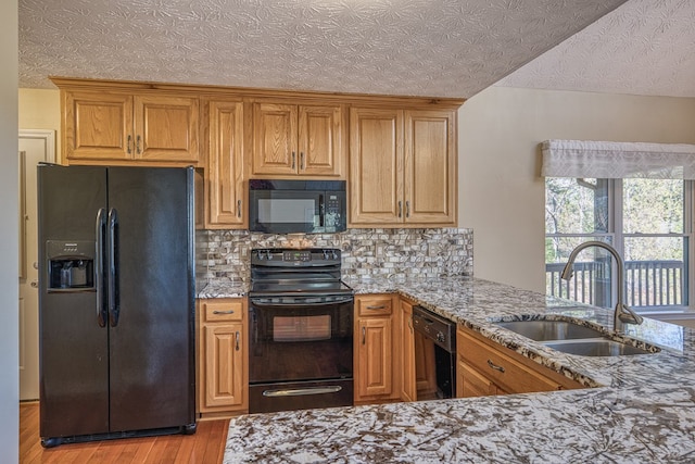 kitchen featuring light stone countertops, light wood-type flooring, tasteful backsplash, black appliances, and a sink