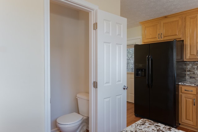 kitchen featuring light wood-style floors, decorative backsplash, light stone counters, and black fridge with ice dispenser