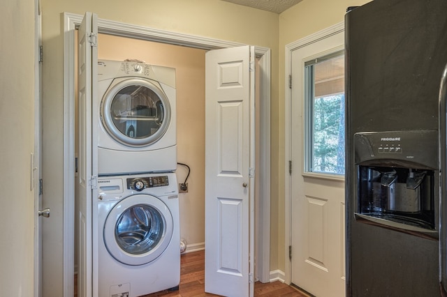 laundry room featuring baseboards, stacked washer and clothes dryer, wood finished floors, and laundry area