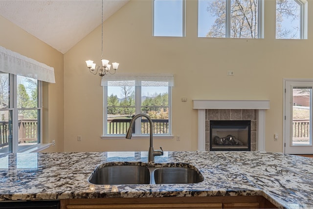kitchen with hanging light fixtures, a sink, a chandelier, stone counters, and high vaulted ceiling