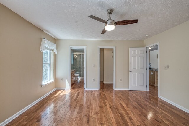 unfurnished bedroom featuring ceiling fan, connected bathroom, a textured ceiling, hardwood / wood-style floors, and baseboards