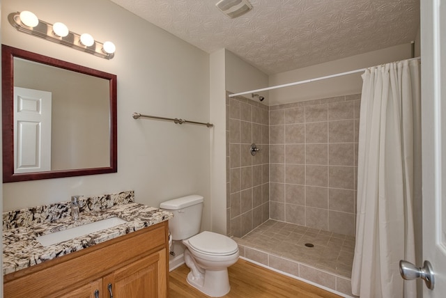 bathroom featuring visible vents, toilet, a tile shower, vanity, and wood finished floors