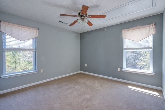 empty room with a ceiling fan, visible vents, carpet floors, attic access, and baseboards