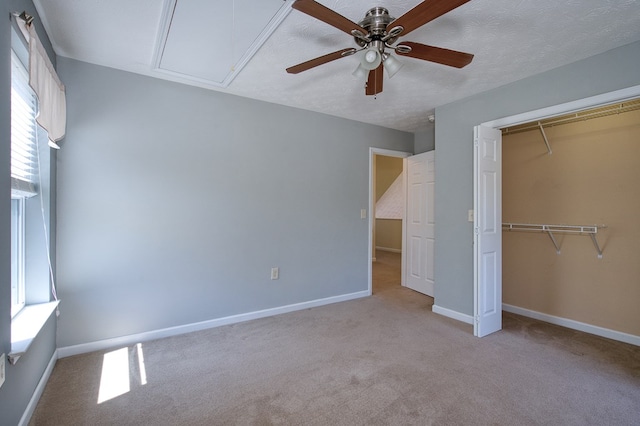 unfurnished bedroom featuring a closet, a ceiling fan, light carpet, attic access, and baseboards