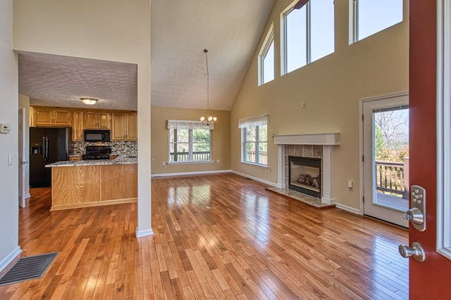 unfurnished living room with baseboards, a high ceiling, a tiled fireplace, a chandelier, and light wood-style flooring