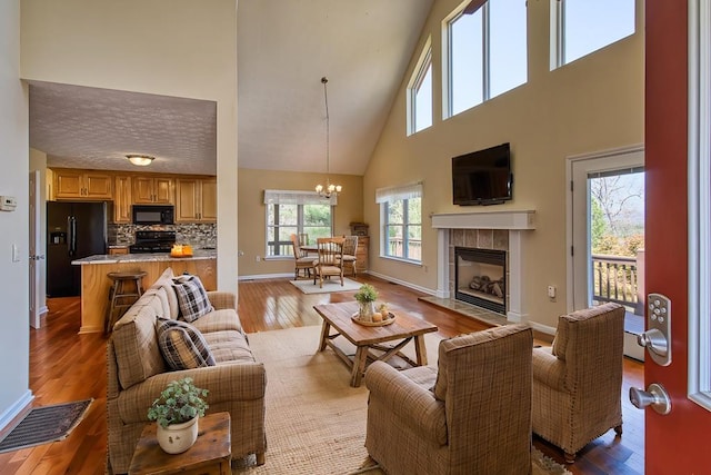 living room featuring baseboards, an inviting chandelier, wood-type flooring, a high ceiling, and a tile fireplace