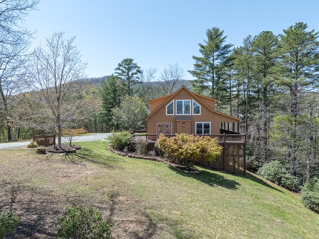 exterior space with a forest view, a wooden deck, and a lawn