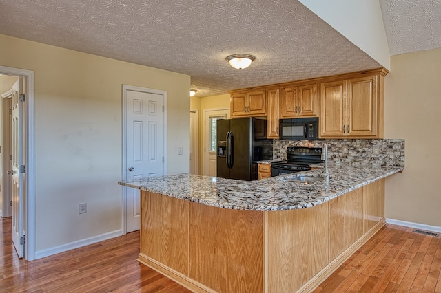 kitchen with baseboards, light stone counters, light wood-style flooring, visible vents, and black appliances