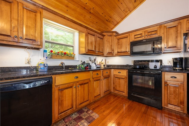 kitchen featuring sink, dark stone countertops, dark hardwood / wood-style floors, black appliances, and vaulted ceiling