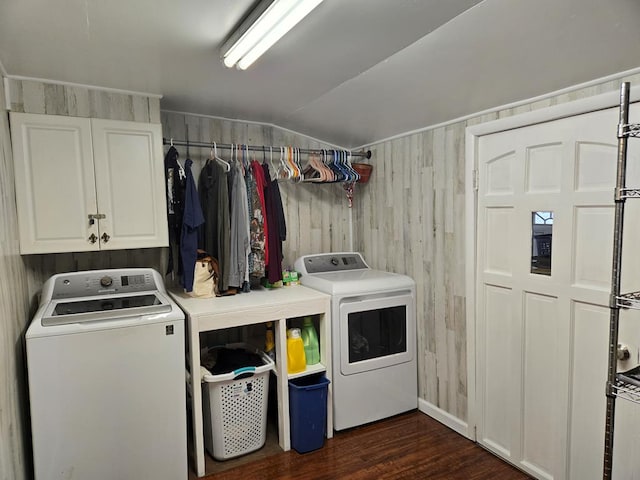 clothes washing area with dark wood finished floors, wood walls, cabinet space, and washer and clothes dryer