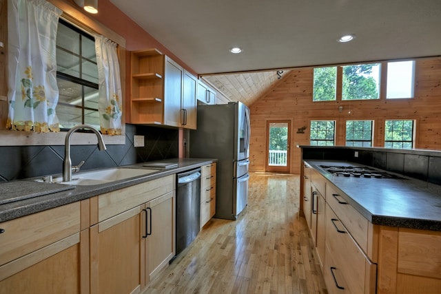 kitchen featuring lofted ceiling, dishwashing machine, wood walls, and a sink