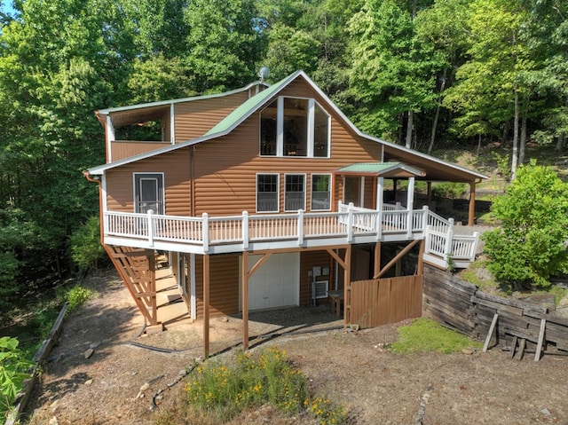 rear view of house with stairs, a deck, a garage, dirt driveway, and faux log siding