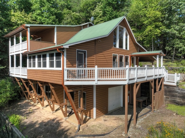 rear view of property featuring a garage, metal roof, a wooden deck, and faux log siding
