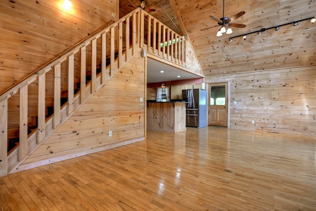 unfurnished living room featuring light wood finished floors, ceiling fan, track lighting, wood ceiling, and wood walls