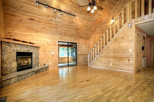unfurnished living room with hardwood / wood-style floors, stairway, wooden walls, and a ceiling fan